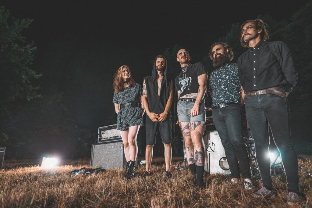 Post-hardcore band Dreamwell, all wearing blue eyeshadow and eyeliner, stand in a row in an empty field at night in front of a drum kit