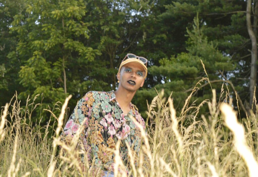 K Nkanza of Spring Silver standing in a field wearing eyeliner and lipstick as photographed by Hannah Dixon