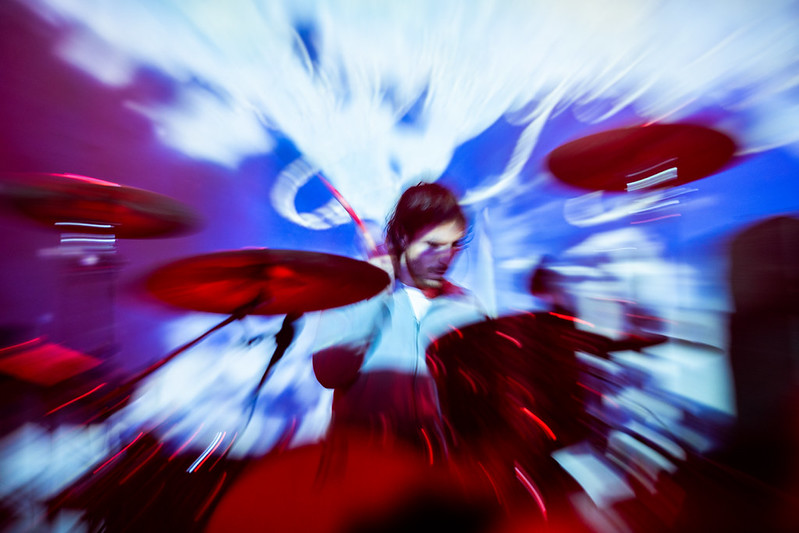 a drummer drums behind a drum kit with a blurry photo effect in place