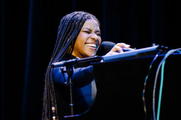 a woman passionately sings into a microphone while playing piano