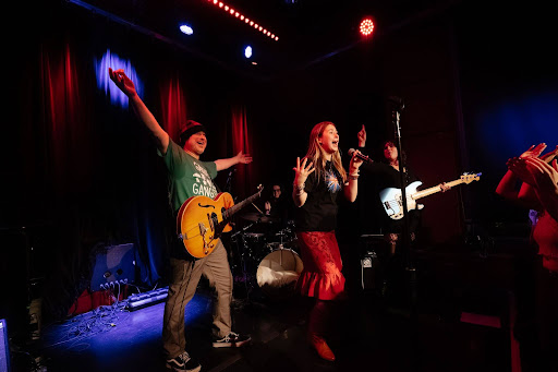 Izzy Pingrey sings into a mic while her guitar player enthusiastically stretches his arms out behind her