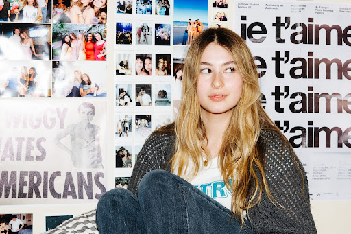 Izzy Pingrey sits in front of a wall covered in posters and photographs